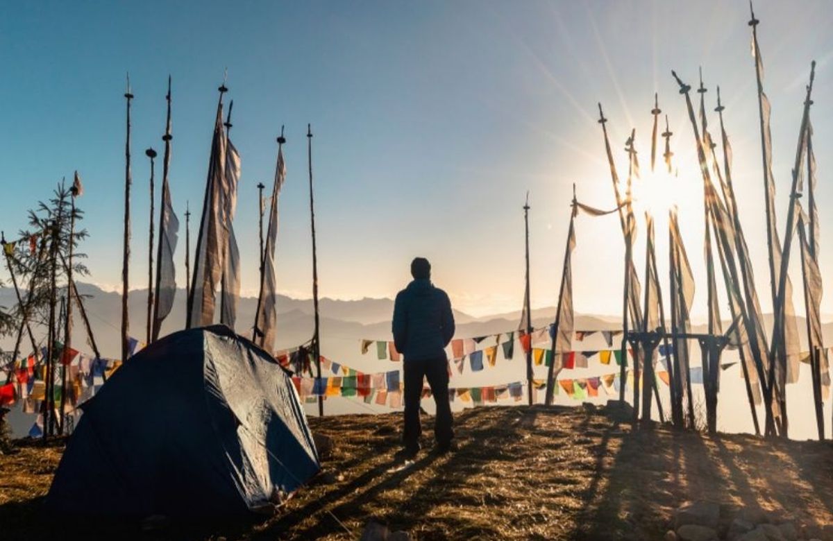 A guide standing among tall prayer-flag poles on a Bhutanese ridge