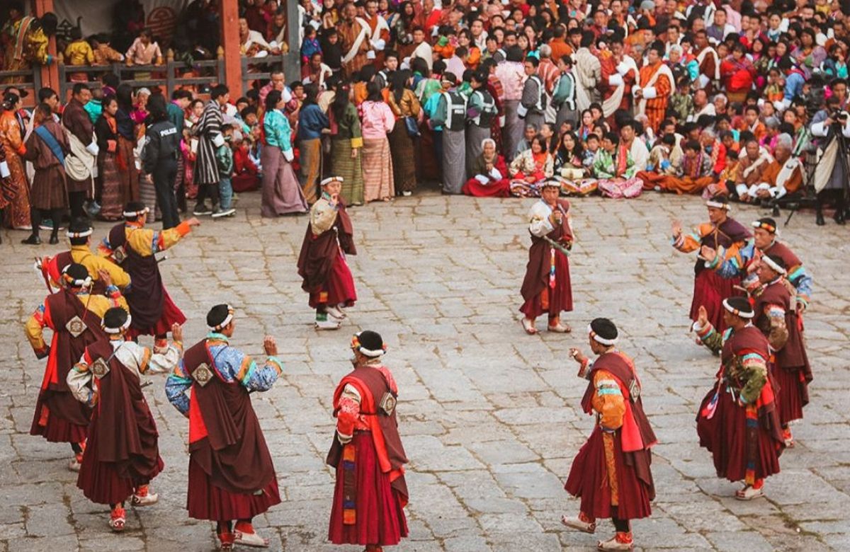 Masked cham dancers performing in a dzong courtyard during a tshechu